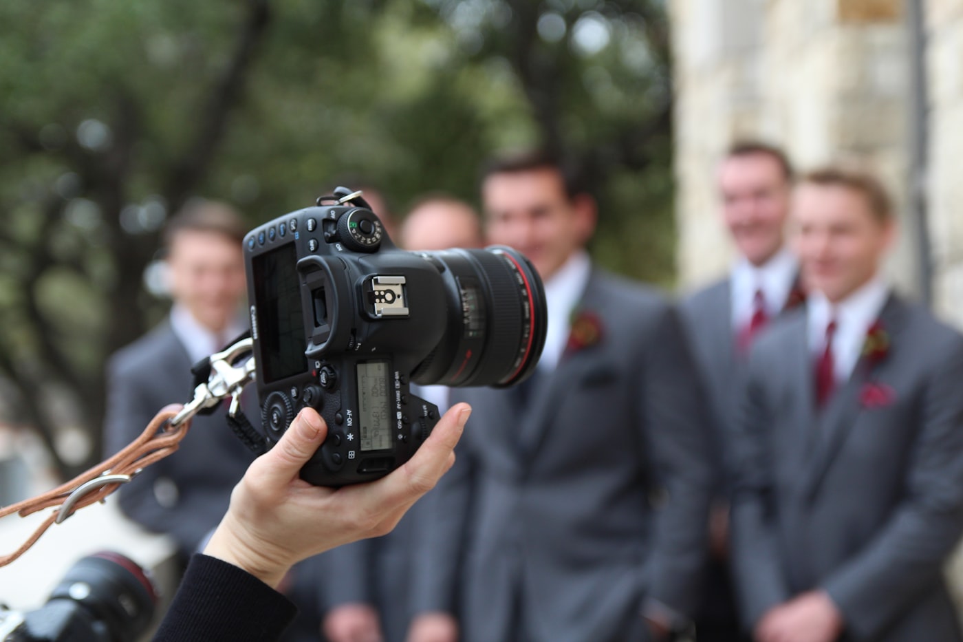 A second shooter's camera in hand, groomsmen soft in the background on a wedding morning
